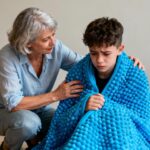 Une professionnelle de santé réconfortant un adolescent autiste en crise avec une couverture sensorielle bleue dans une pièce calme