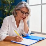 Femme dans la cinquantaine concentrée sur un test cognitif avec cahier bleu et crayon jaune dans un bureau professionnel