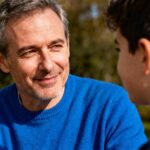 Homme de 50 ans portant un pull bleu vif échangeant un regard bienveillant dans un contexte de sensibilisation à l'autisme
