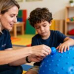 Thérapeute européen accompagnant un enfant autiste avec des outils de thérapie bleus dans une pièce naturelle et chaleureuse
